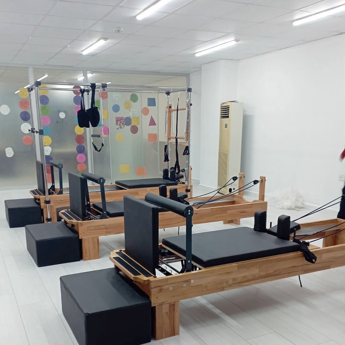 Stüdyoda yan yana dizilmiş ahşap gövdeli basic reformerler ve arkada metal kafesli Cadillac reformer