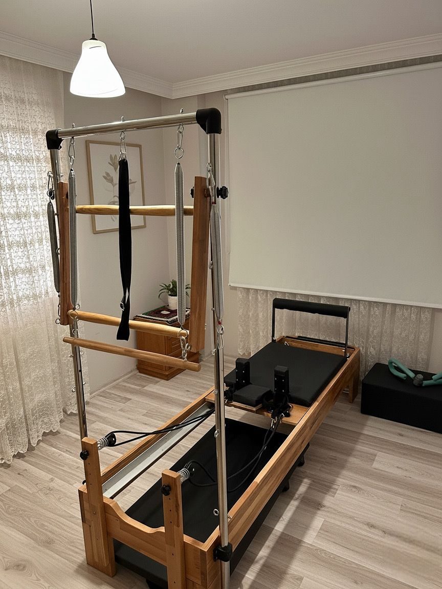 Ev odasında kurulu ahşap gövdeli tower reformer; metal kulede yaylar, ahşap barlar ve askı bandı