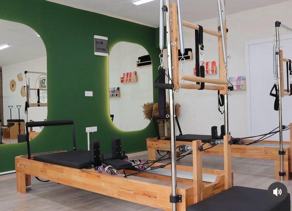 Yeşil duvarlı pilates stüdyosunda yan yana kurulu tower reformerler ve oval aynalar